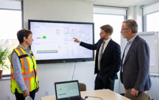 Three professionals reviewing a dashboard display showing how municipal workflows get digitized with GIS maps and data analytics.